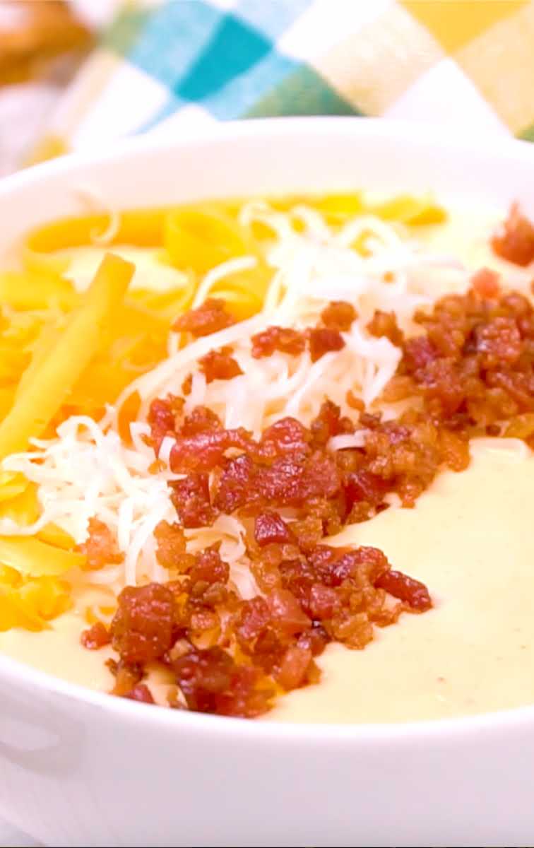 close up shot of a condiment bowl of Beer cheese dip topped with shredded cheese and bacon bits