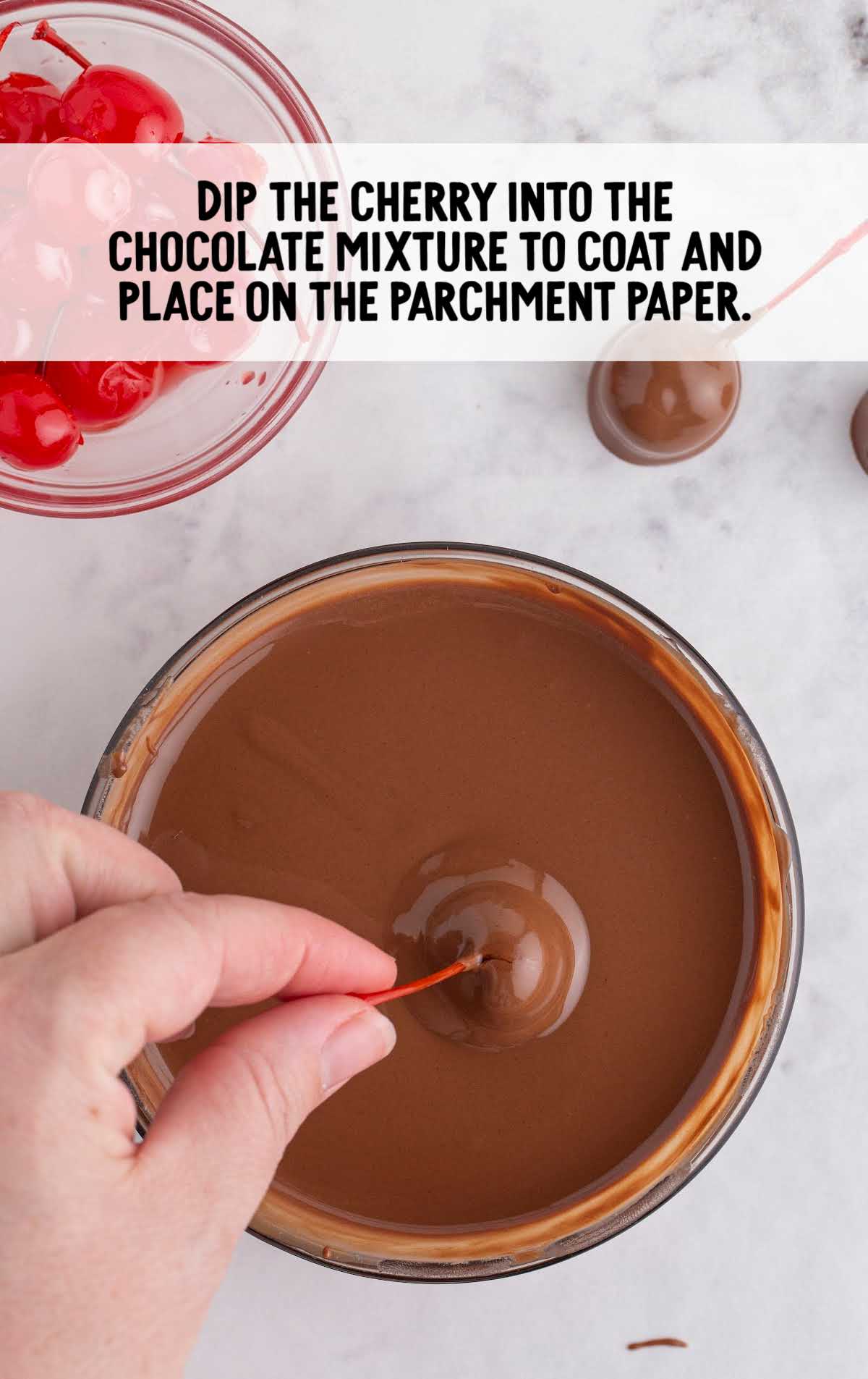 a maraschino cherry dipped into the bowl of melted chocolate