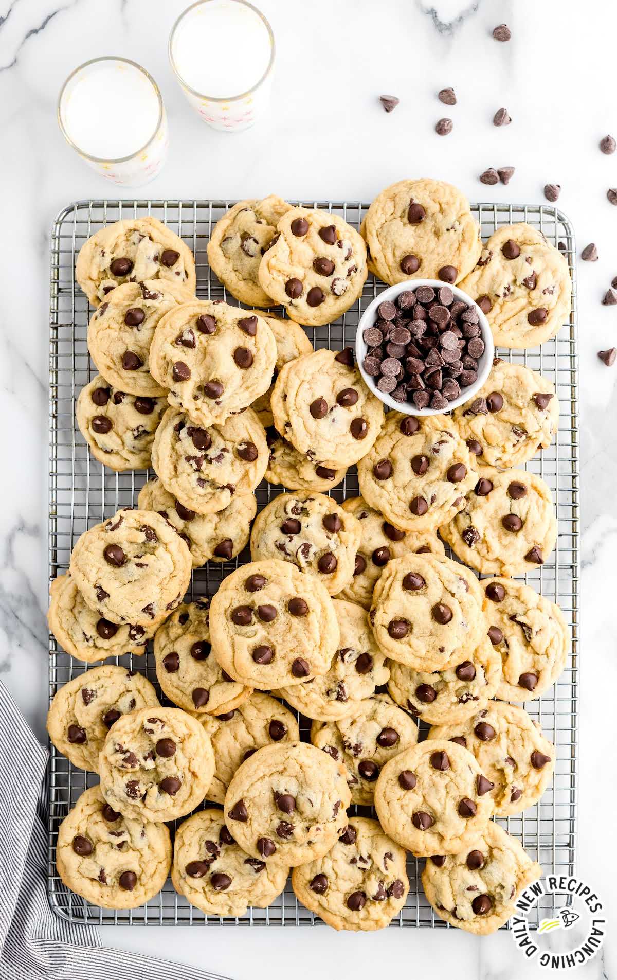 overhead shot of Chocolate Chip Pudding Cookies piled on a cooling rack with a bowl of chocolate chips