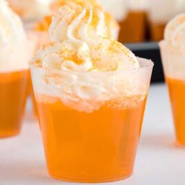 close up shot of shot cups of Creamsicle Jello Shot topped with whipped cream and garnished with orange sprinkles