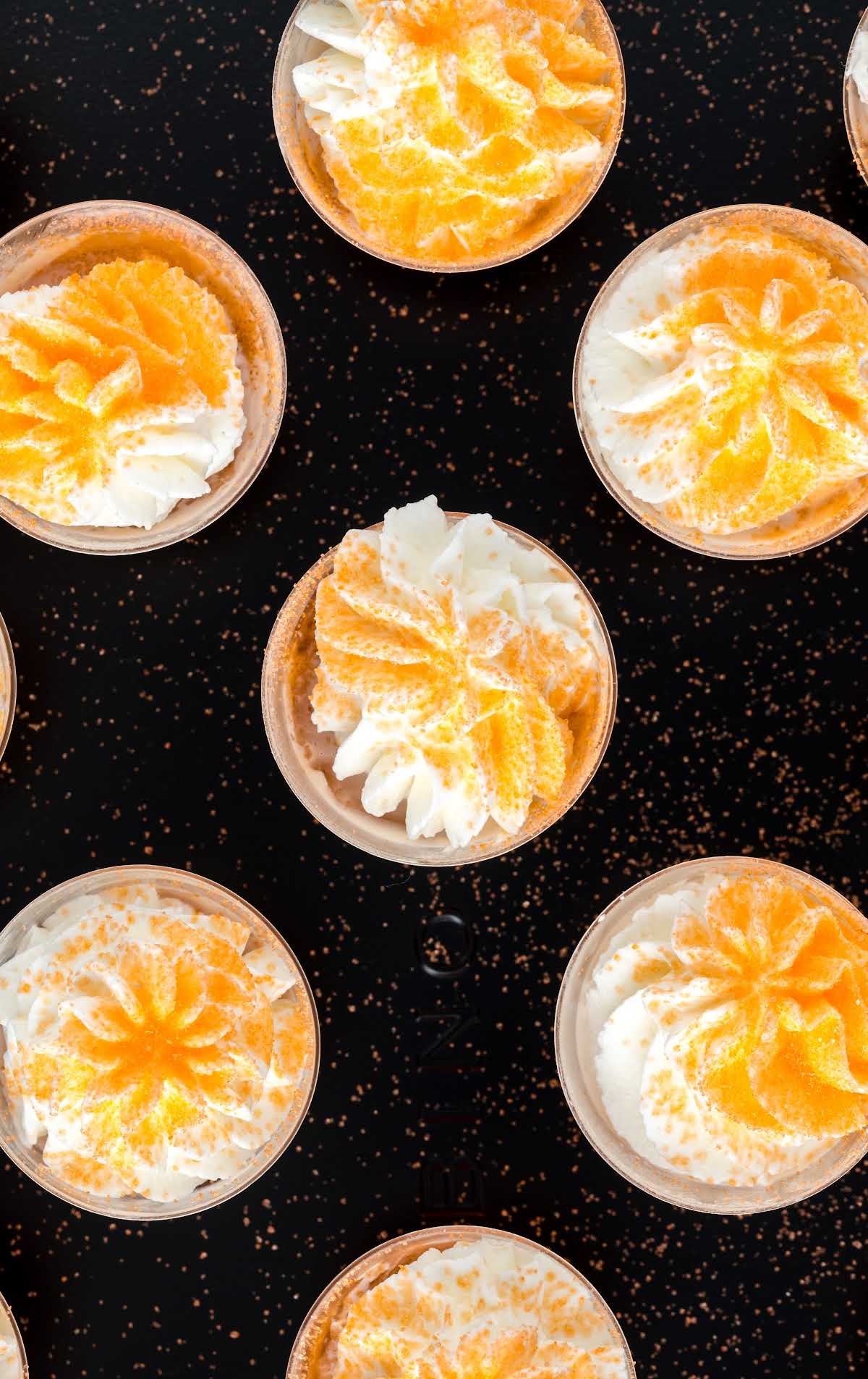 close up overhead shot of shot cups of Creamsicle Jello Shot topped with whipped cream and garnished with orange sprinkles