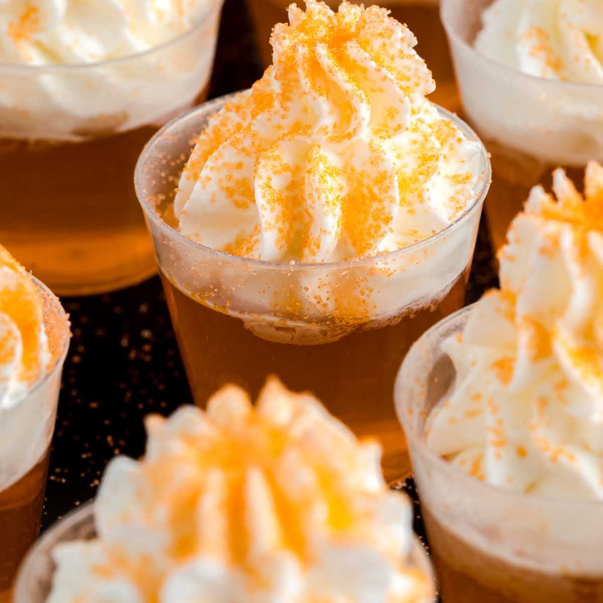 close up shot of shot cups of Creamsicle Jello Shot topped with whipped cream and garnished with orange sprinkles