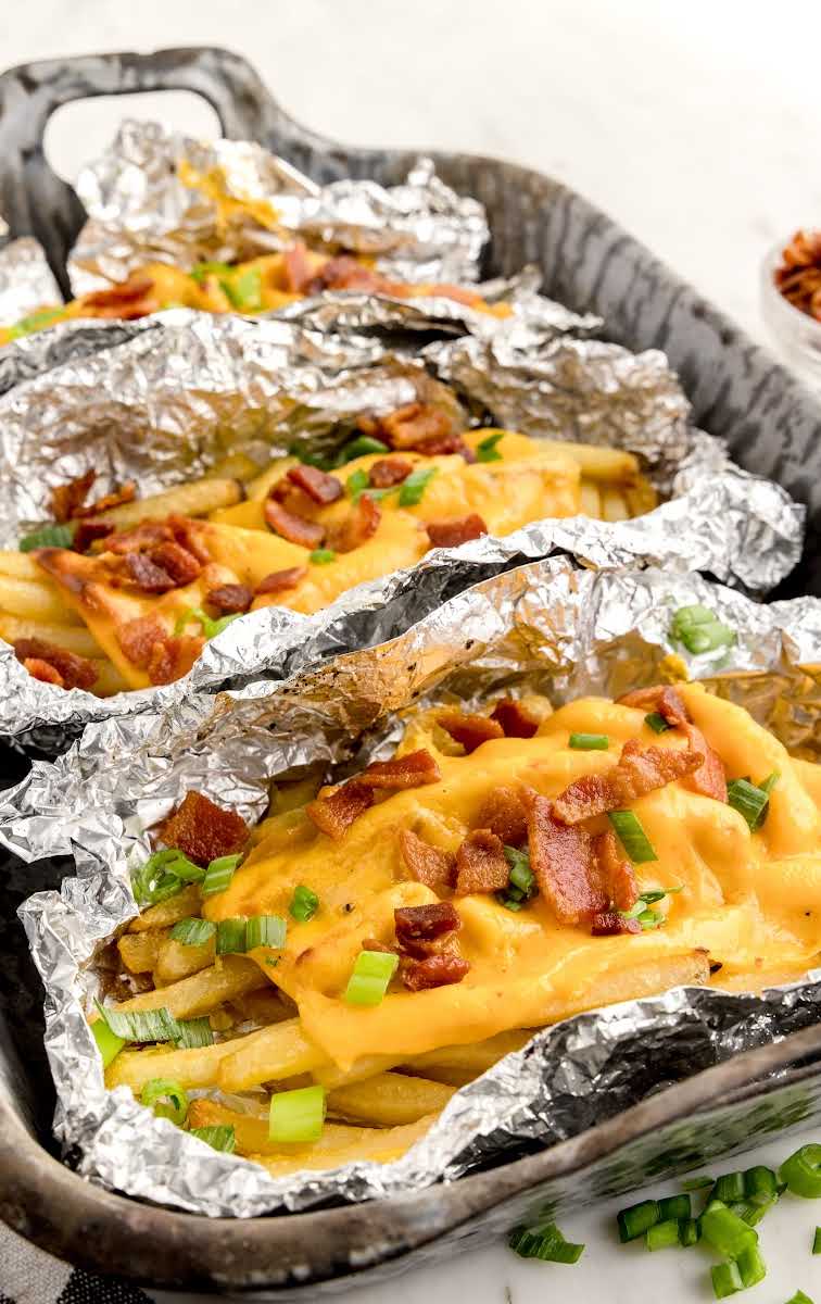 close up shot of aluminum foils of Dirty Fries topped with cheese then garnished with bacon bits and green onions