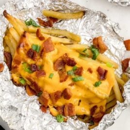 close up overhead shot of a aluminum foil of Dirty Fries topped with cheese then garnished with bacon bits and green onions