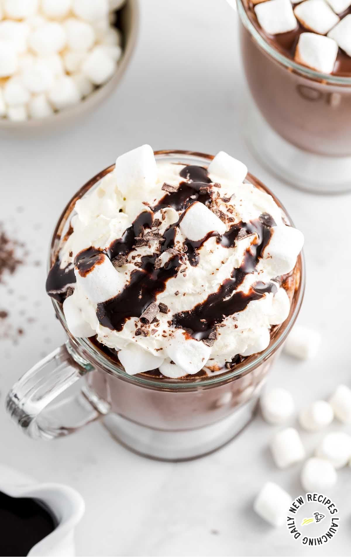 close up shot of a glass of Homemade Hot Chocolate topped with whipped cream, marshmallows, chocolate shavings, and chocolate syrup