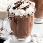 close up shot of a glass of Homemade Hot Chocolate topped with whipped cream, marshmallows, chocolate shavings, and chocolate syrup