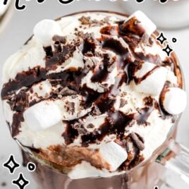 close up shot of a glass of Homemade Hot Chocolate topped with whipped cream, marshmallows, chocolate shavings, and chocolate syrup