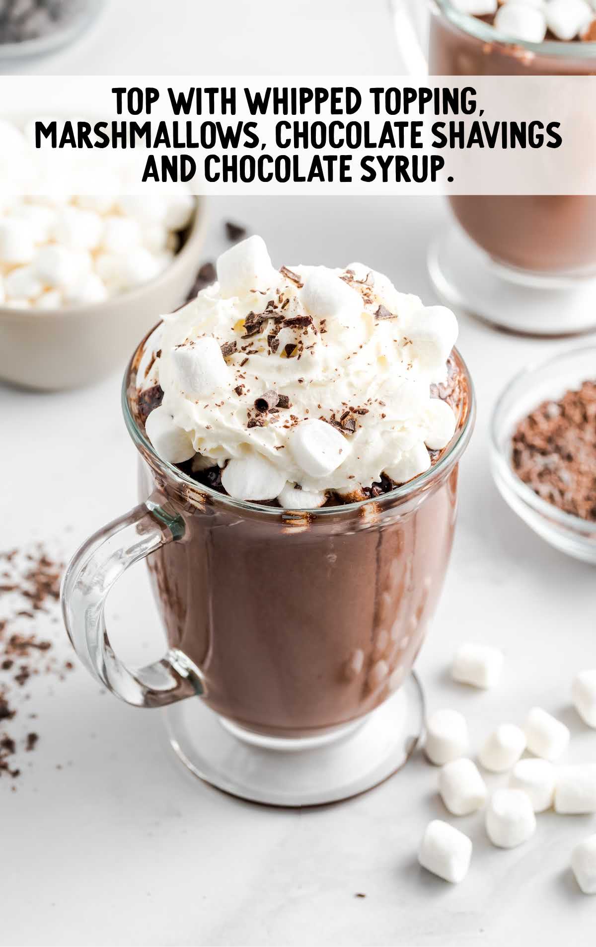 a glass of Hot Chocolate topped with whipped cream, marshmallows, chocolate shavings, and chocolate syrup