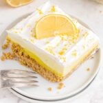 close up shot of a slice of No-Bake Lemon Pie garnished with lemon peel and a slice of lemon on a plate with a fork