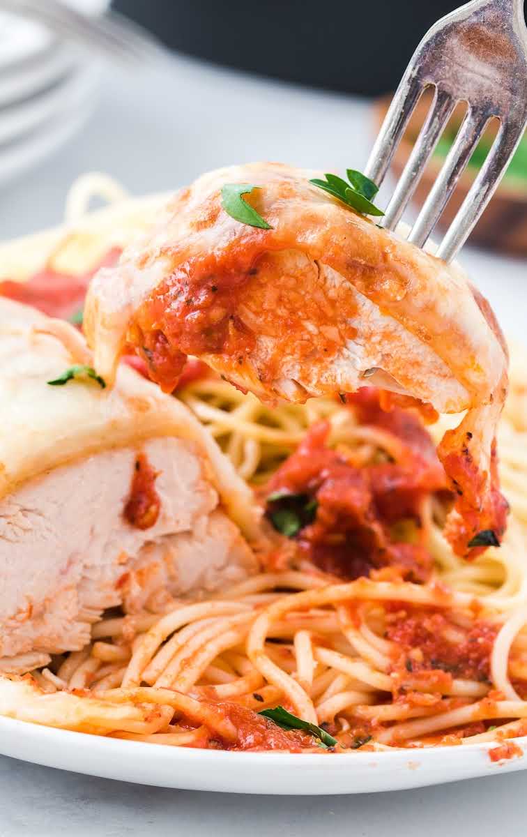 close up shot of a plate of Skillet Chicken And Mozzarella Bake garnished with parsley and served over spaghetti noodles