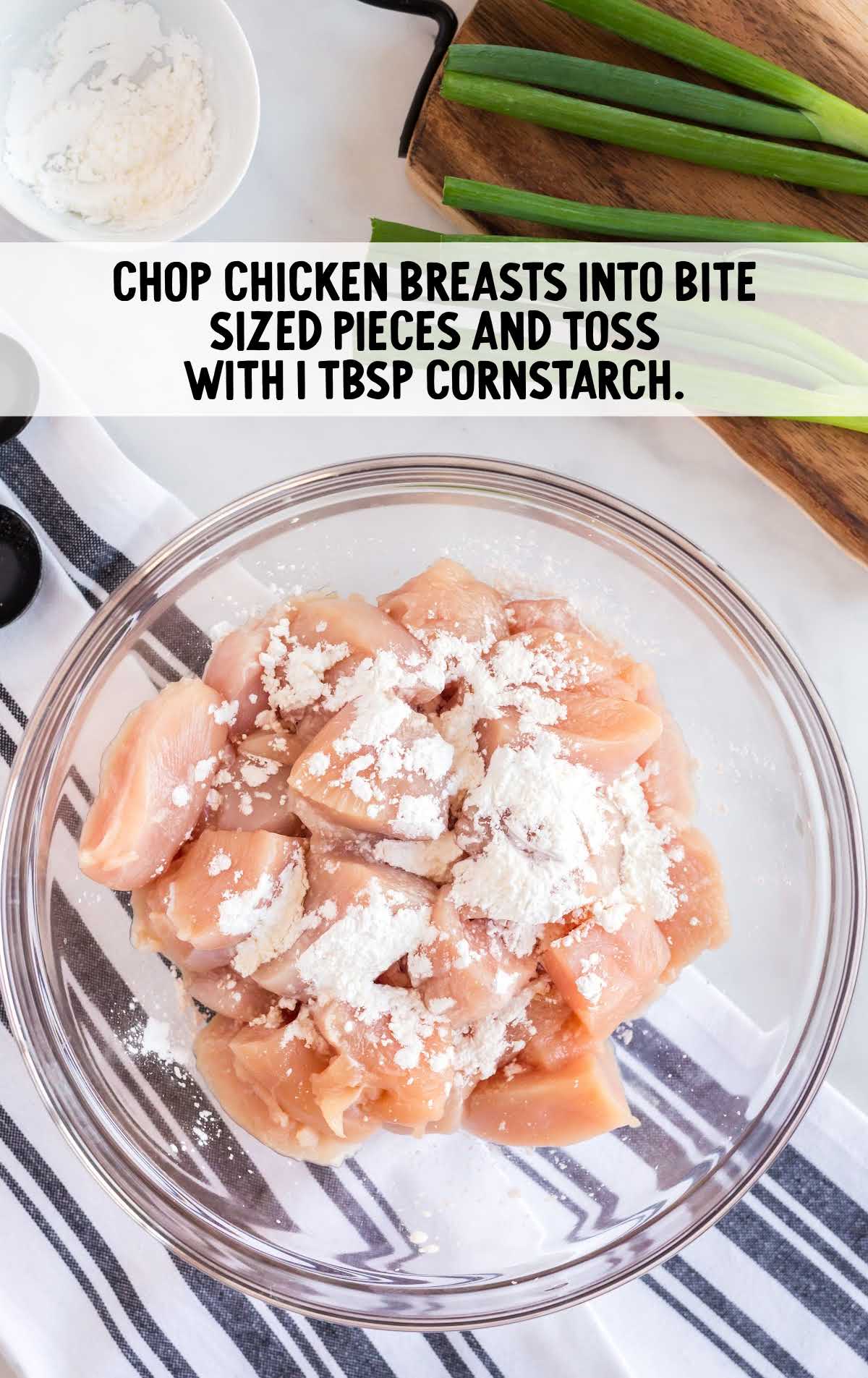 chopped chicken breast being tossed in cornstarch in a clear bowl