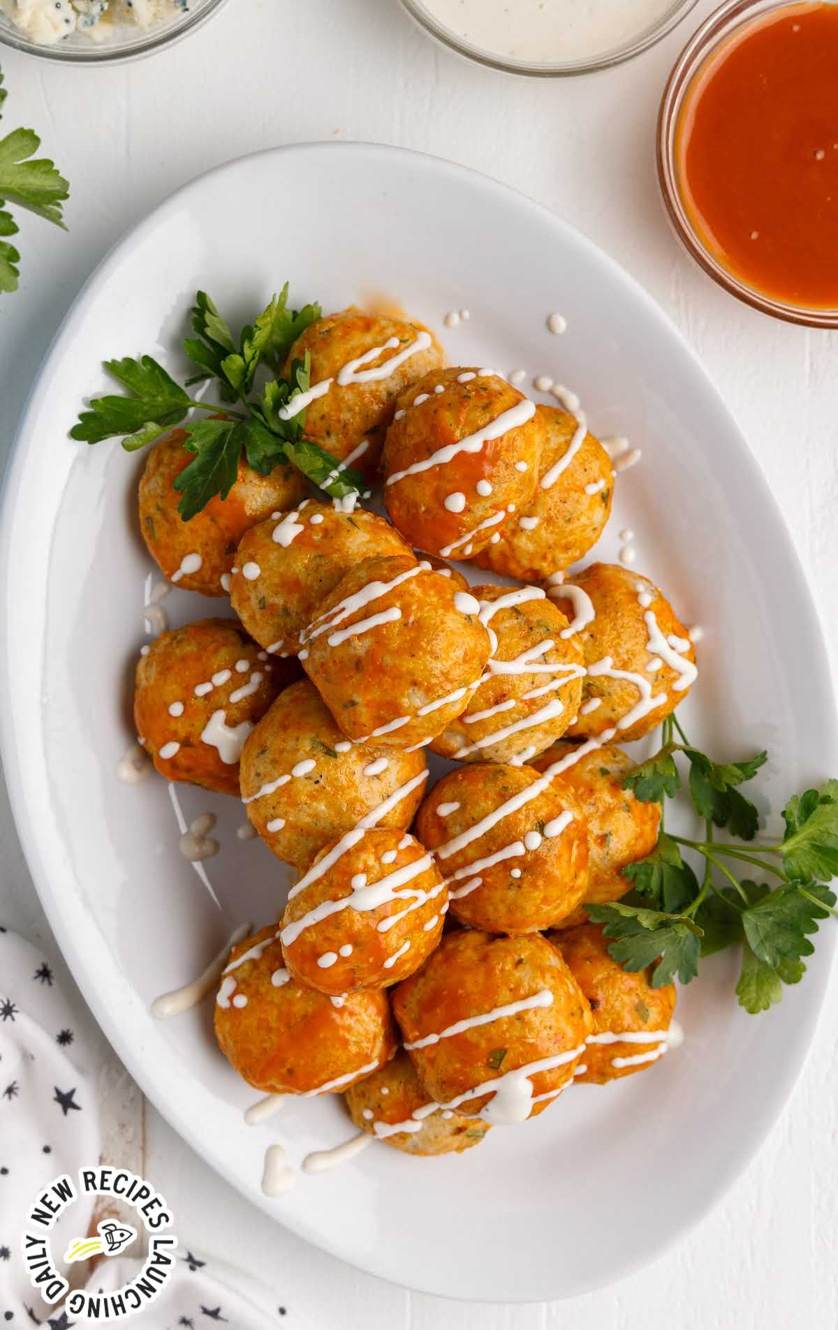 overhead shot of a plate of Buffalo Chicken Meatballs drizzled with buffalo sauce and ranch dressing and sprinkled with parsley and blue cheese crumbles