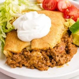 close up shot of a plate of Crescent Roll Taco Bake topped with sour cream and served with tomatoes, lettuce, and avocado