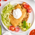 close up overhead shot of a plate of Crescent Roll Taco Bake topped with sour cream and served with tomatoes, lettuce, and avocado