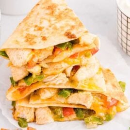 close up shot of Fajita Quesadillas stacked on top of each other with a side of guacamole and sour cream