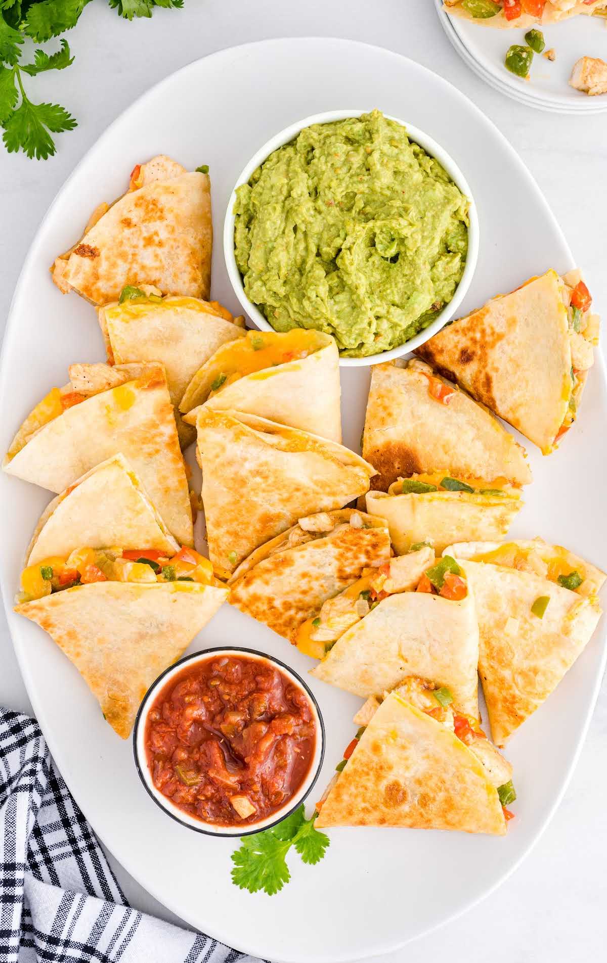 close up overhead shot of Fajita Quesadillas on a serving tray with sides of guacamole and salsa