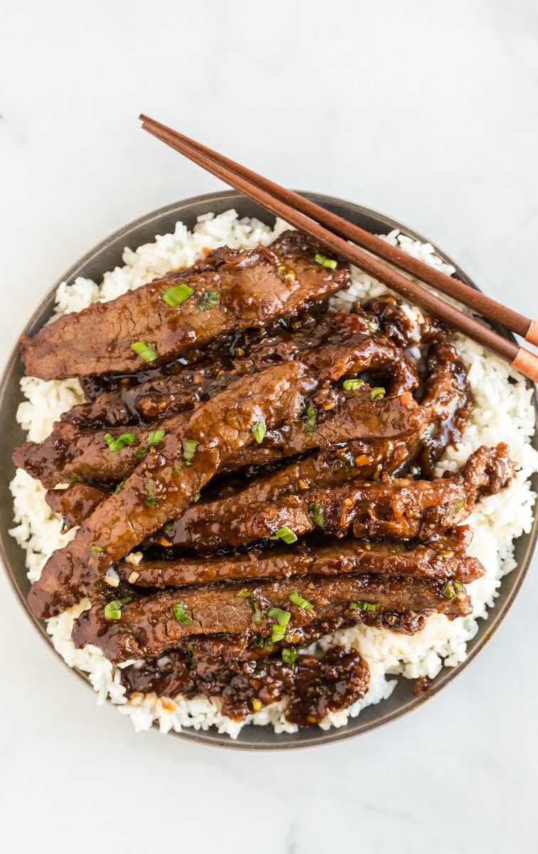 close up overhead shot of a plate of Mongolian Beef garnished with green onions and served over white rice with chopsticks