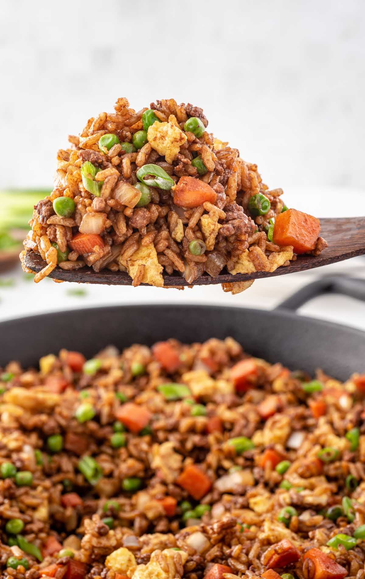 close up shot of a spoonful of pork fried rice hovering over a skillet of Pork Fried Rice