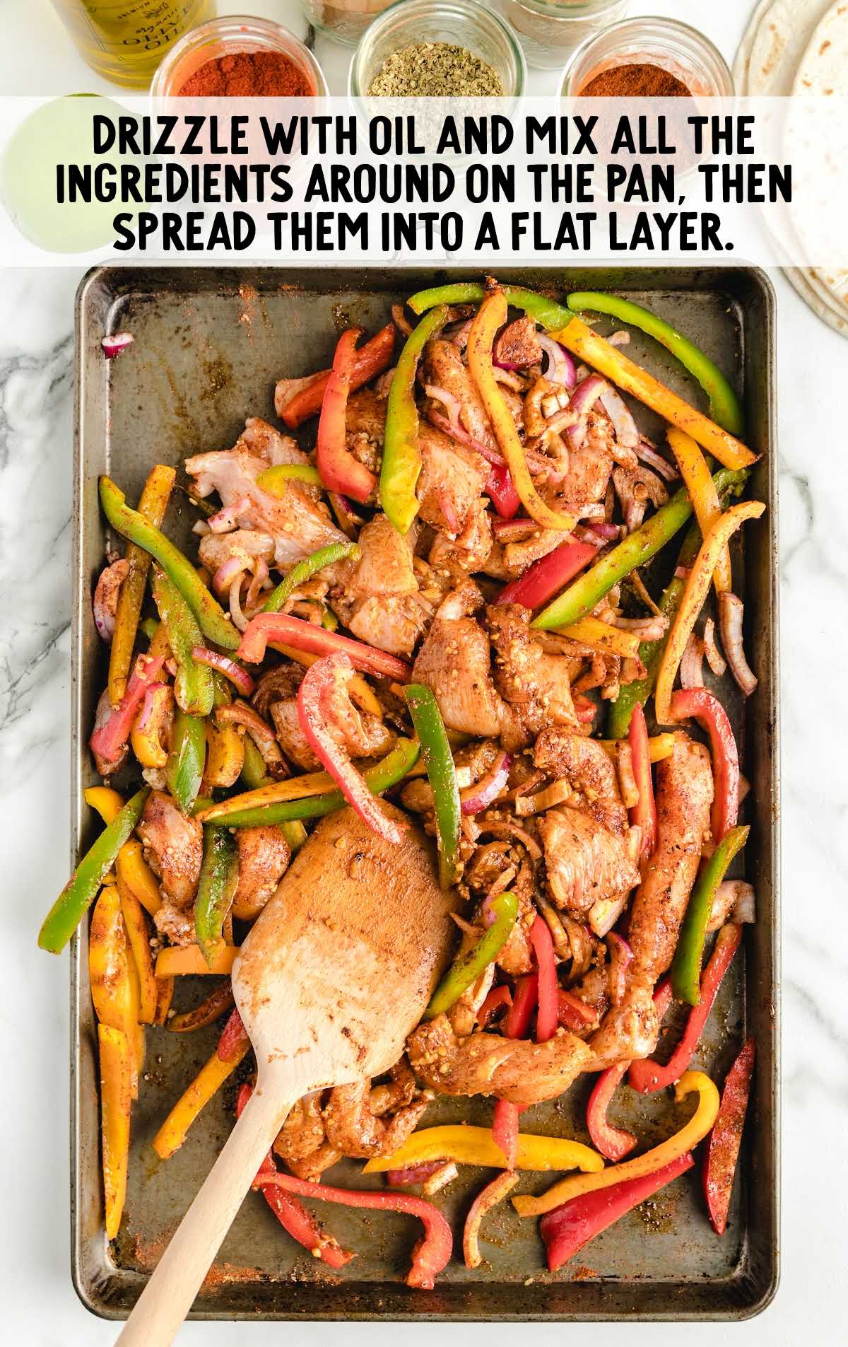 Fajitas ingredients drizzled with oil and mixed around on a sheet pan