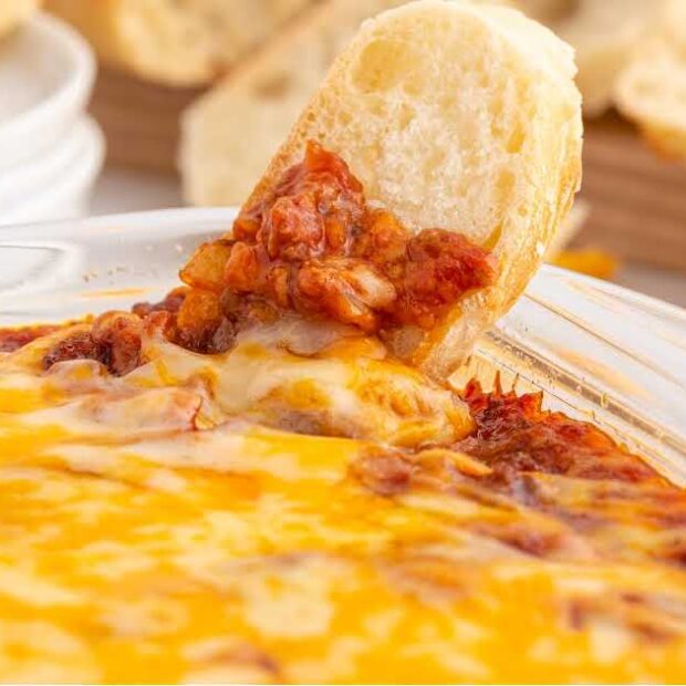close up shot of a baking dish full of Sloppy Joe Dip with a French baguette dipped into it