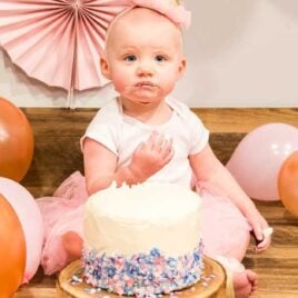 a baby girl eating a Smash Cake with balloons all around