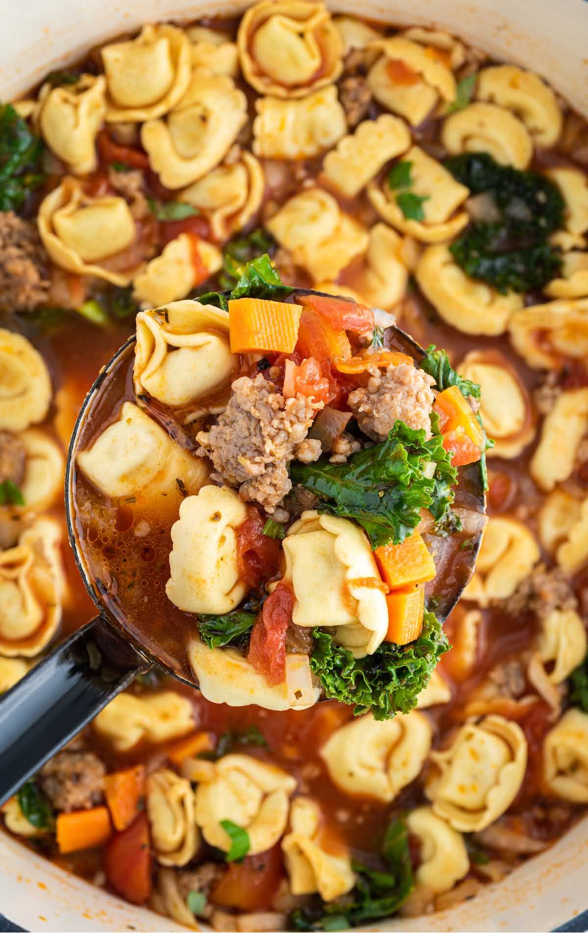 close up overhead shot of a spoonful of tortellini soup hovering over a pot of Tortellini Soup