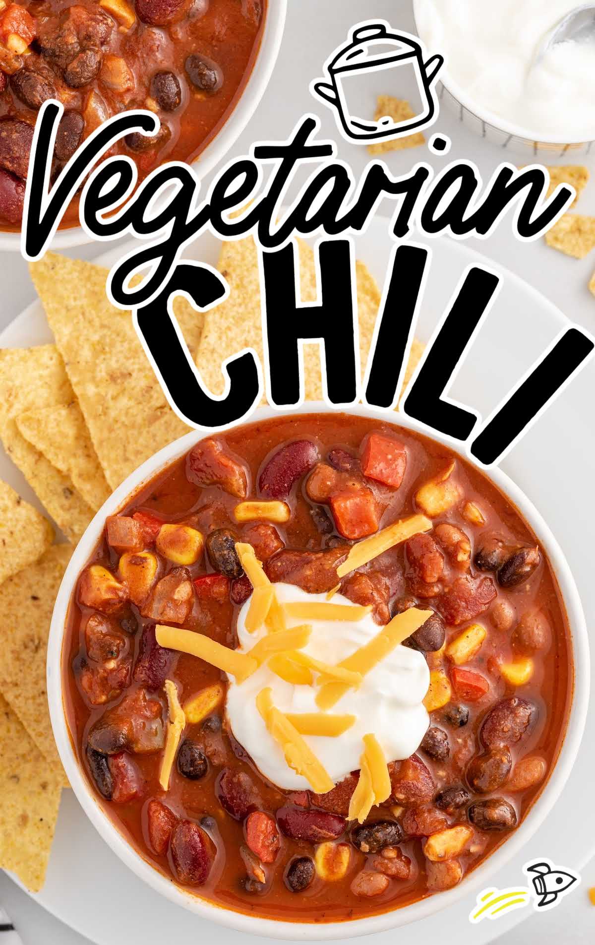 overhead shot of a bowl of Vegetarian Chili topped with sour cream and shredded cheese then placed on a plate of tortilla chips