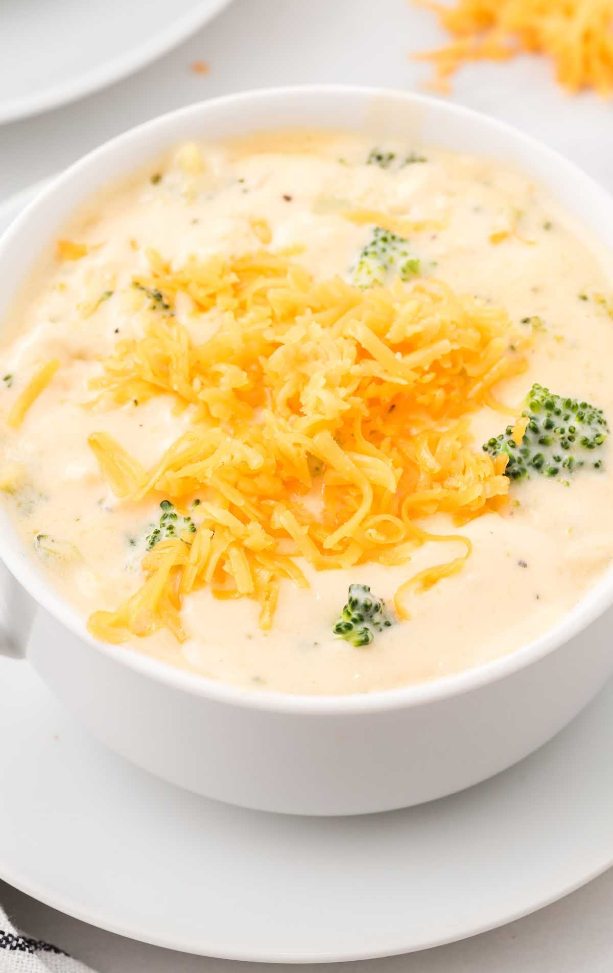 close up shot of a bowl of broccoli and cheese soup topped with shredded cheese