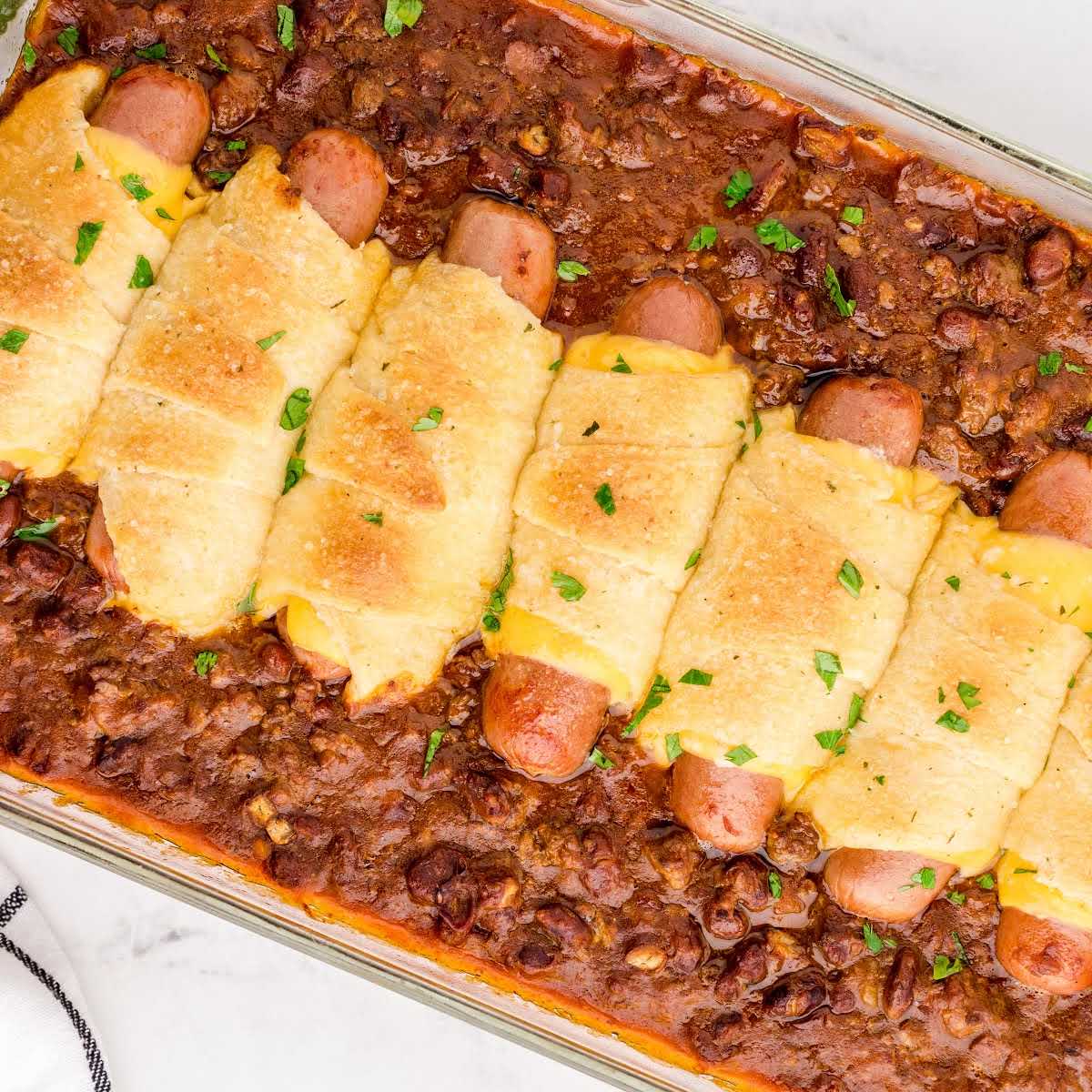 close up overhead shot of a baking dish of chili cheese dog bake garnished with parsley