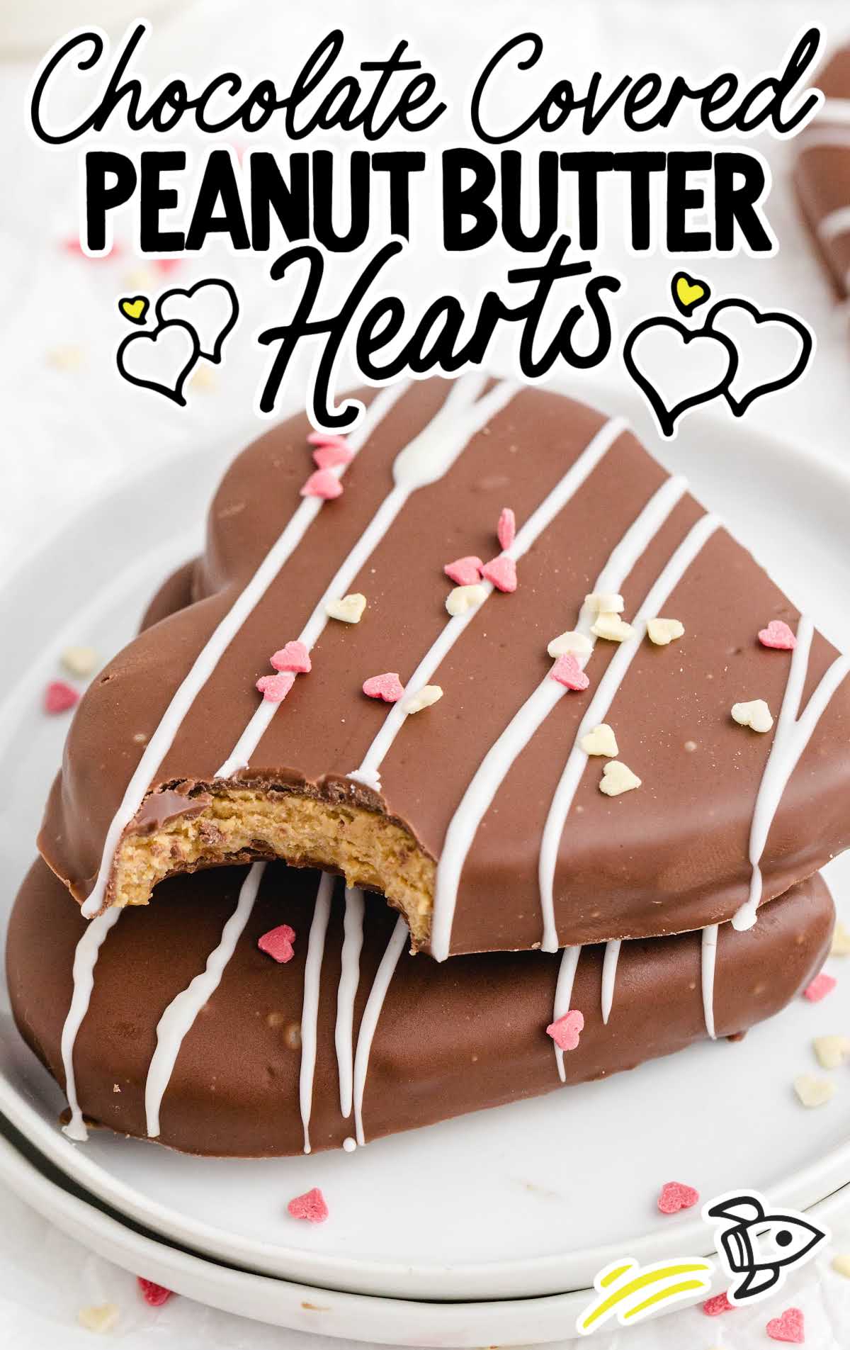 close up shot of a plate of chocolate covered peanut butter hearts drizzled with white chocolate and topped with heart sprinkles