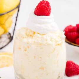 close up shot of a cup of lemon fluff topped with whipped topping and a raspberry