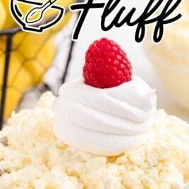 close up shot of a bowl of lemon fluff topped with whipped topping and a raspberry