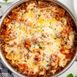 Overhead view of skillet lasagna in a stainless steel pan with golden melted cheese and garnished with herbs.