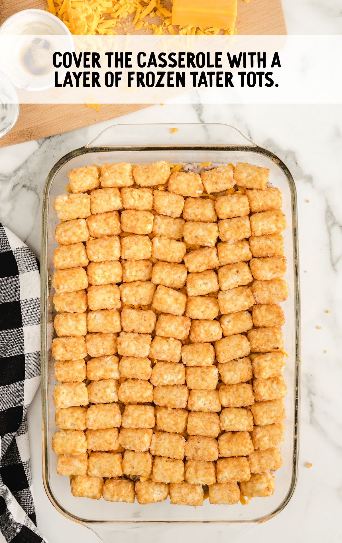 tater tot casserole process shot of shredded cheese topped with tater tots in a baking dish