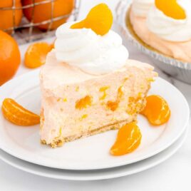 close up shot of a slice of pie topped with whipped cream and a mandarin orange on a plate