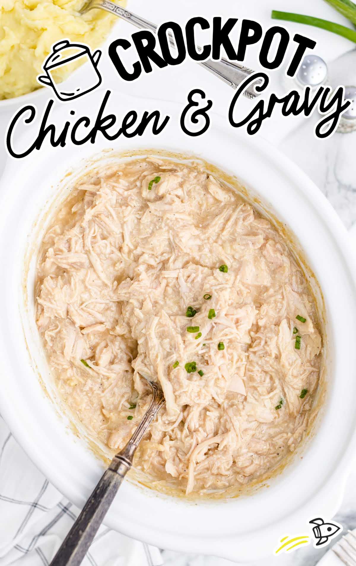 overhead shot of a crockpot full of chicken and gravy garnished with green onions