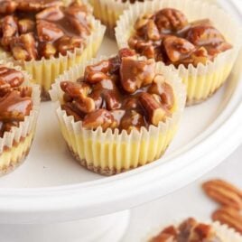 close up shot of a serving stand of cheesecake bites topped with pecans