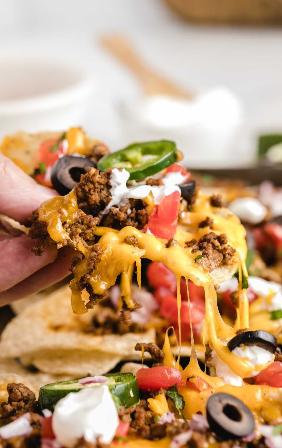 close up shot of a handful of Sheet Pan Nachos garnished with toppings
