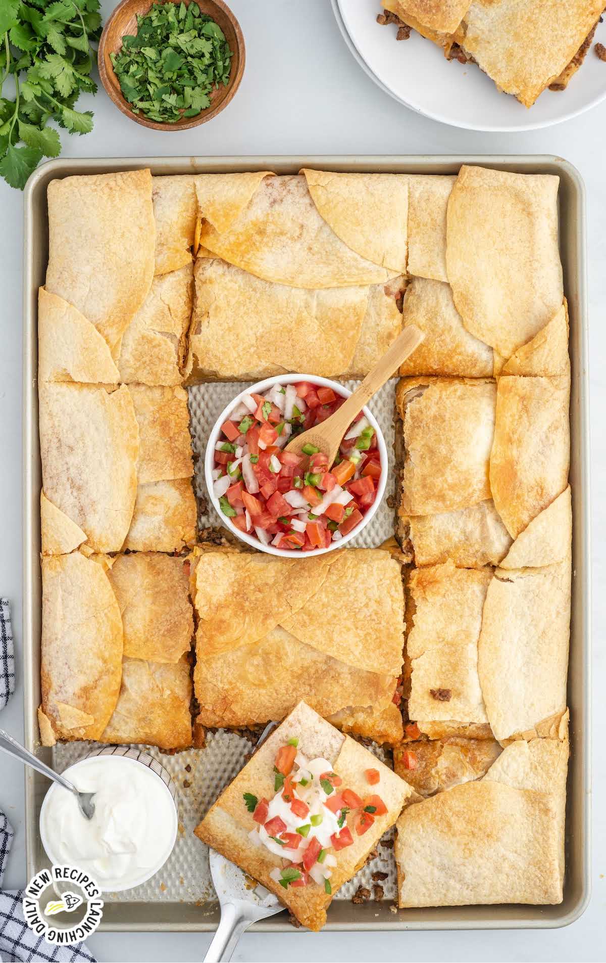overhead shot of sheet pan full of tacos with a bowl of salsa and cream cheese