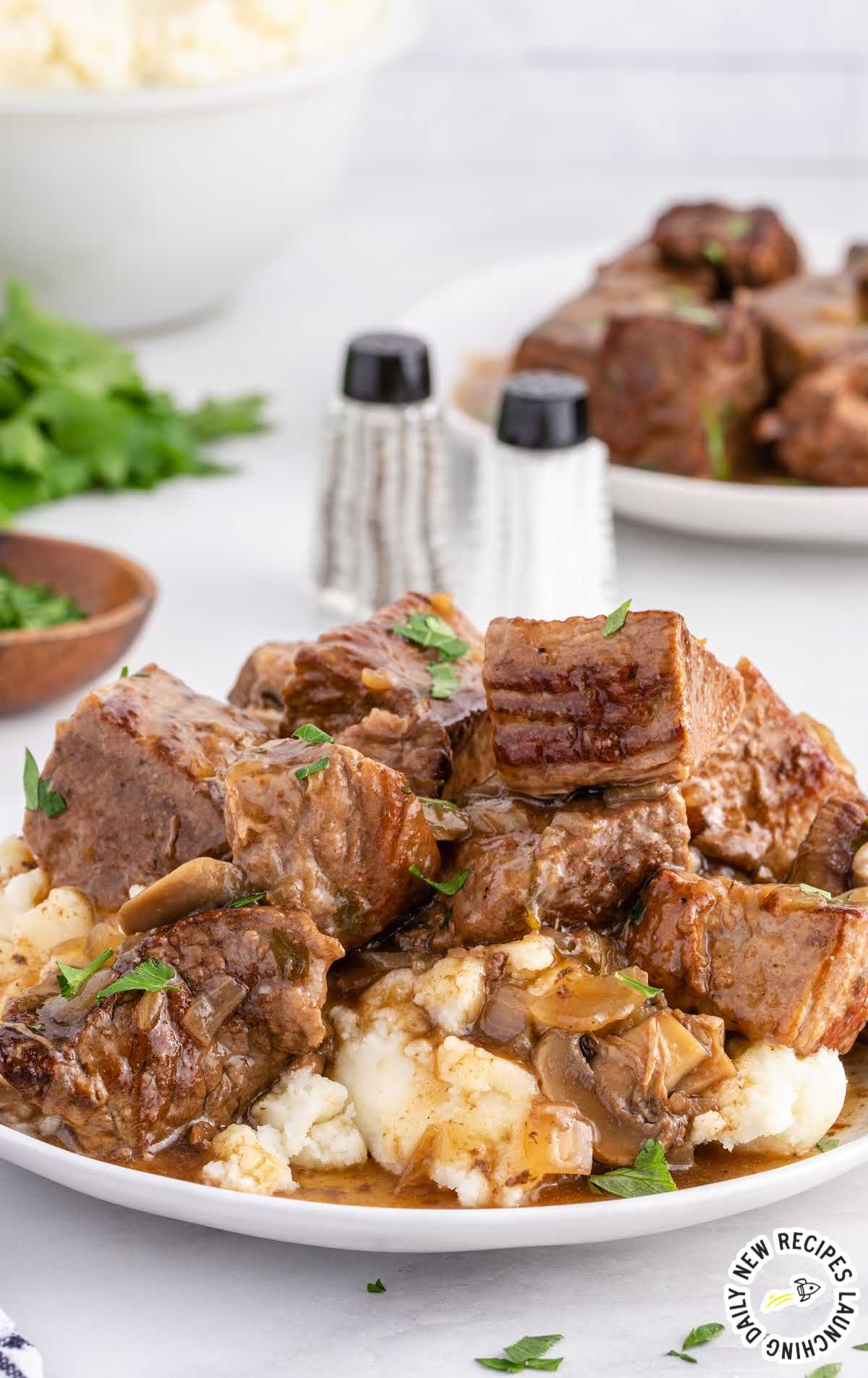 close up shot of a plate of beef tips garnished with parsley and served over mashed potatoes