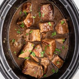 close up overhead shot of a slow cooker full of beef tips garnished with parsley