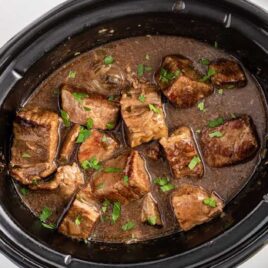 overhead shot of a slow cooker full of beef tips garnished with parsley