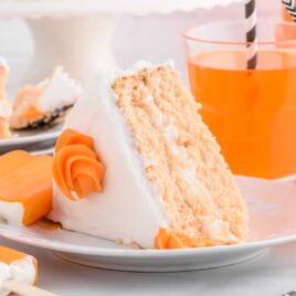 a slice of cake topped with frosting on a plate surrounded by cups of orange soda