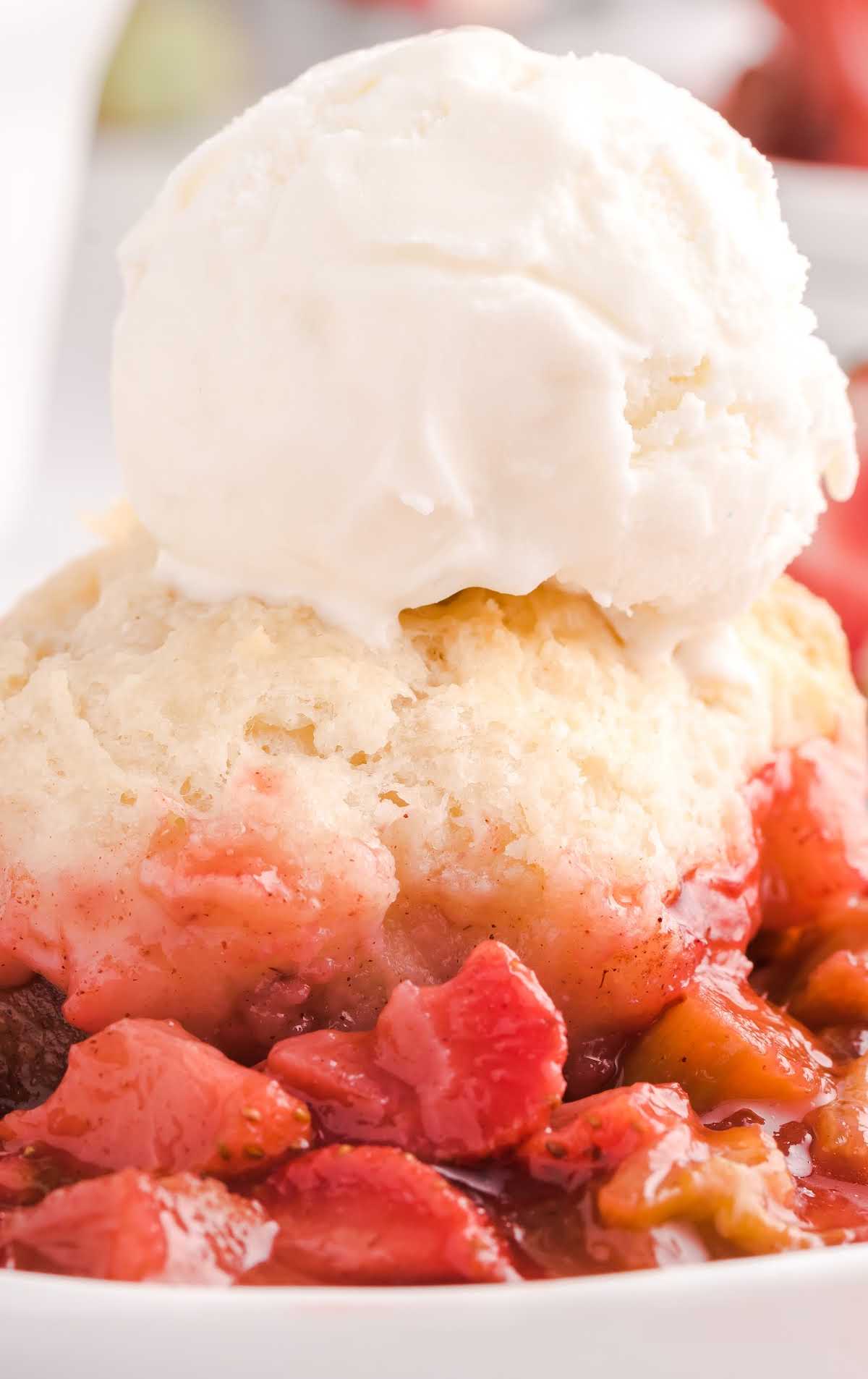 close up shot of a piece of Rhubarb Cobbler topped with vanilla ice cream on a plate