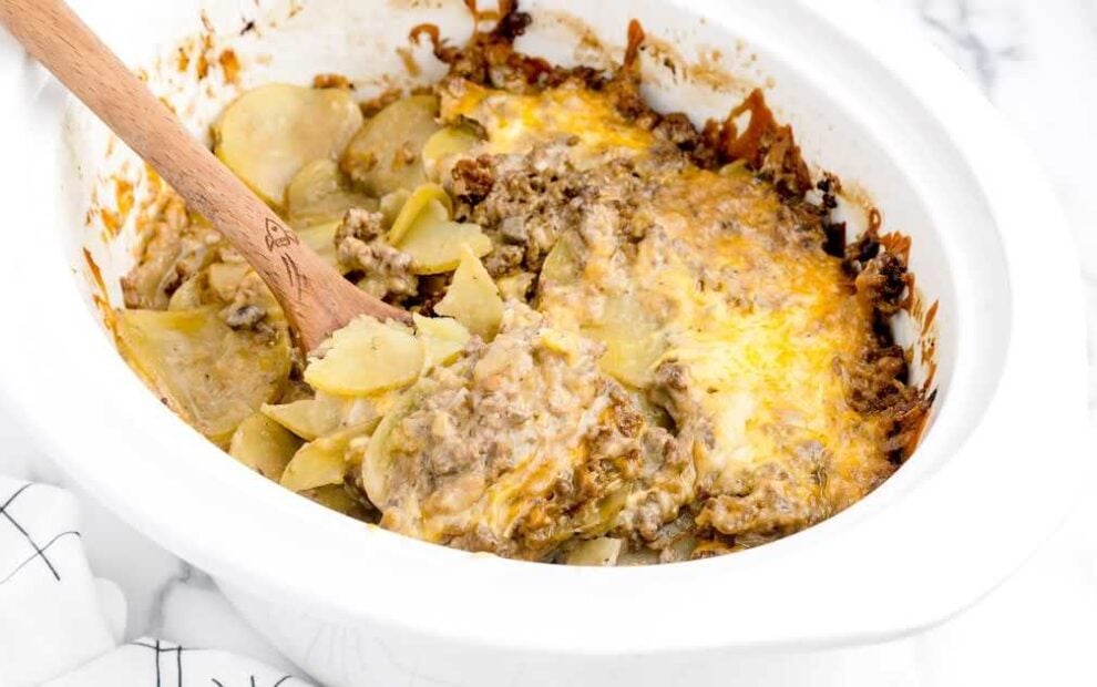close up shot of a slow cooker full of beef and potatoes with a large wooden spoon