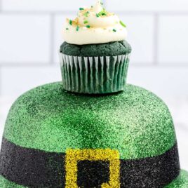 close up shot of a frosted cupcake topped with sprinkles on top of a st. Patrick's day hat