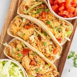 close up overhead shot of a wooden serving tray of slow cooker queso chicken tacos drizzled with sauce