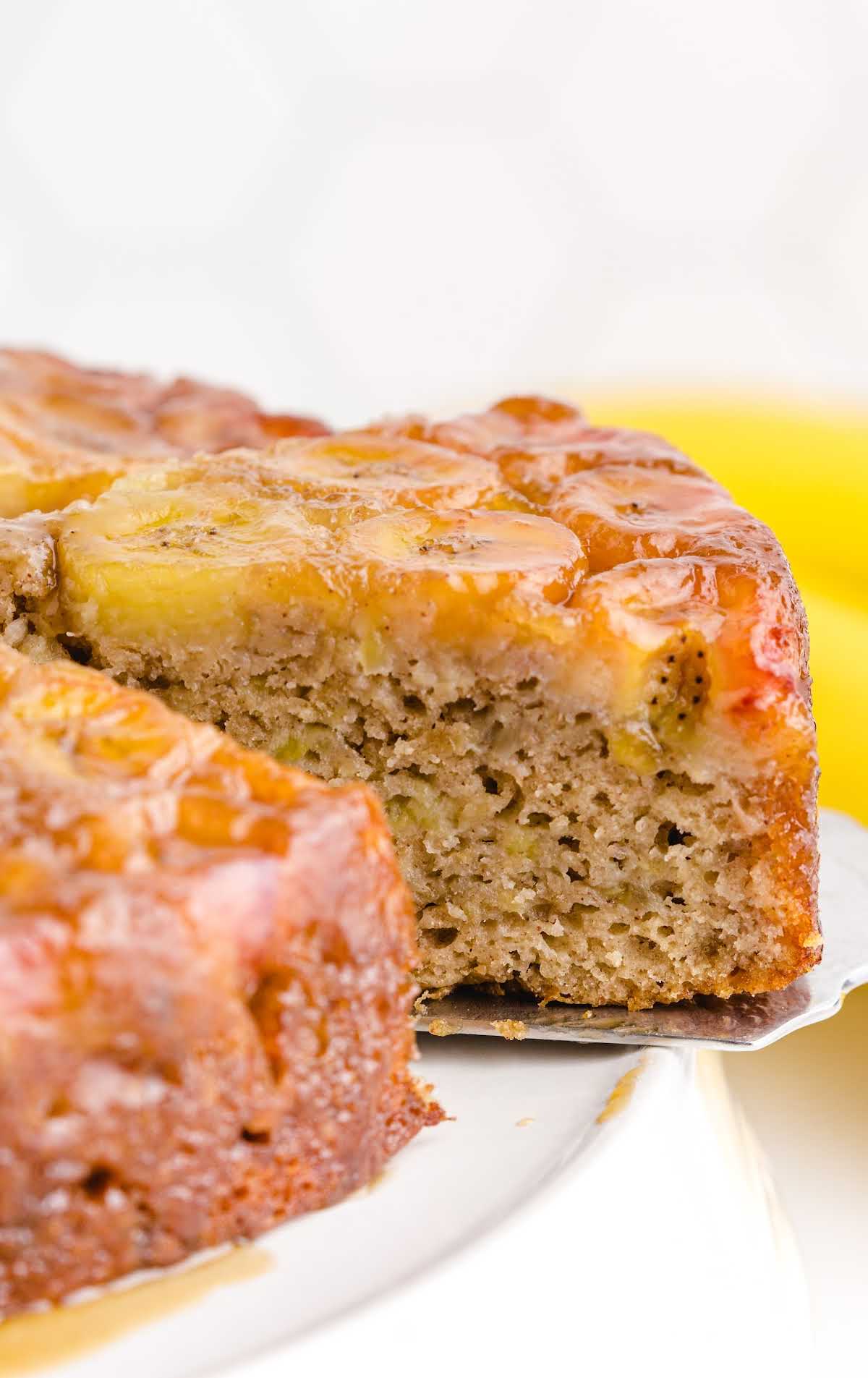 close up shot of a Banana Upside-Down Cake on a cake stand with a slice being removed with a spatula