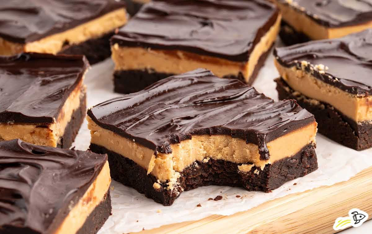 Several buckeye brownies arranged on parchment paper, with one brownie missing a bite to reveal the creamy peanut butter filling.