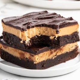 Two stacked buckeye brownies on a white plate, with rich chocolate, thick peanut butter layer, and glossy ganache topping.